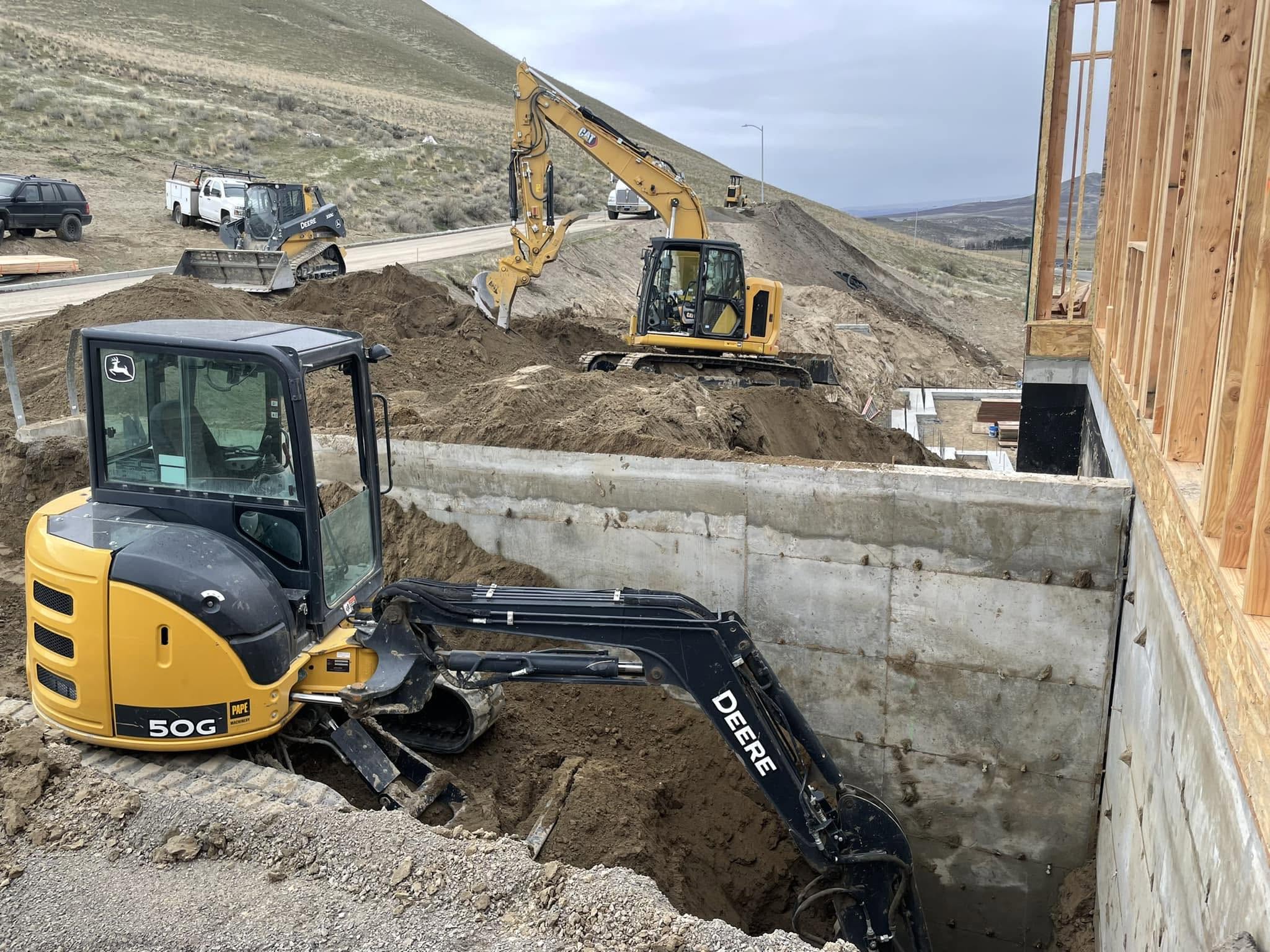 John Deere excavators digging a building foundation against a concrete wall